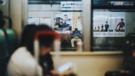 一位中年男子边玩手机边候车。在日本，老式翻盖手机在中老年人群市场中经久不衰。而它早已被坐在列车里的年轻人遗弃。