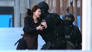 A woman runs to police officers after she escaped a hostage situation at a Sydney cafe on Monday, December 15. The siege ended with the death of the gunman and two of his hostages, but questions remain unanswered.