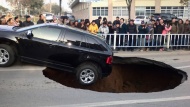 People in Zhenjiang, China, watch a car dangle on the edge of a giant sinkhole on Friday, December 12